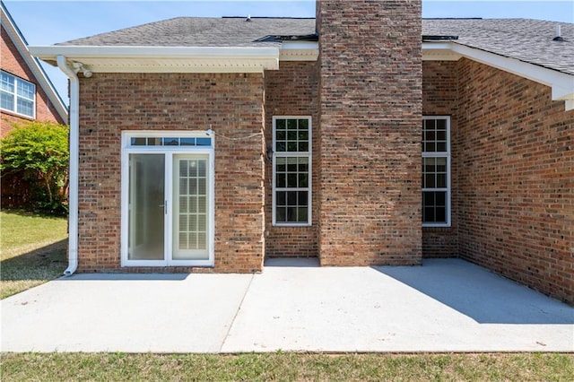 back of property with a chimney, brick siding, a patio area, and a shingled roof