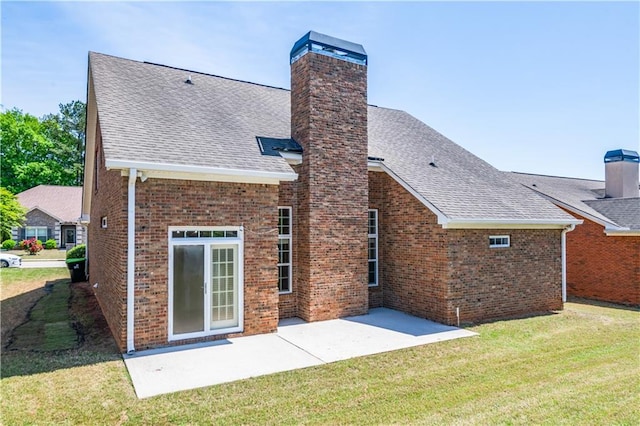 back of property with a chimney, roof with shingles, a patio area, and a lawn
