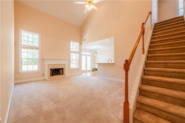 unfurnished living room featuring a fireplace with flush hearth, stairs, baseboards, and ceiling fan with notable chandelier