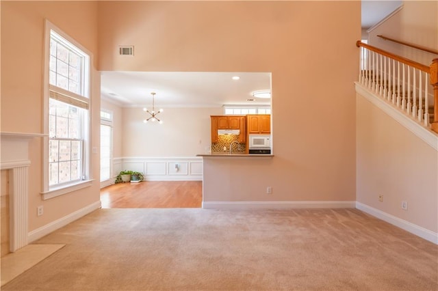 unfurnished living room featuring visible vents, light carpet, a sink, baseboards, and a notable chandelier