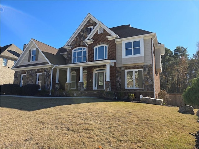 view of front facade with a front yard, a porch, fence, and stone siding