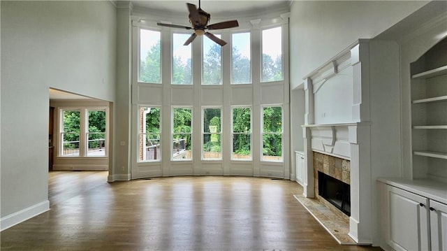 unfurnished living room with a fireplace with flush hearth, dark wood-style flooring, a towering ceiling, and ceiling fan