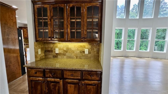 kitchen featuring glass insert cabinets, light stone countertops, dark brown cabinetry, decorative backsplash, and wood finished floors