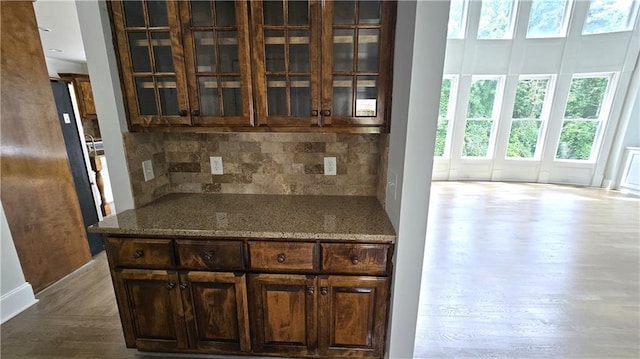 kitchen with decorative backsplash, glass insert cabinets, dark wood-style floors, and stone countertops