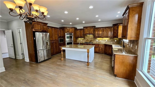 kitchen featuring an inviting chandelier, light wood-style flooring, a kitchen island with sink, a sink, and stainless steel appliances