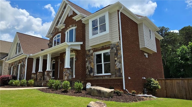 view of property exterior featuring brick siding, fence, a porch, a lawn, and stone siding