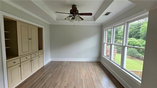 unfurnished room with a ceiling fan, wood finished floors, baseboards, crown molding, and a raised ceiling