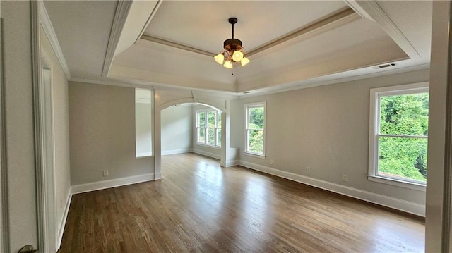 empty room with crown molding, wood finished floors, arched walkways, a raised ceiling, and a ceiling fan