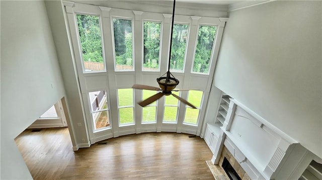 unfurnished living room with wood finished floors, a ceiling fan, visible vents, a fireplace, and a towering ceiling