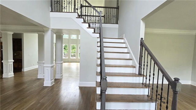 stairs featuring crown molding, baseboards, decorative columns, a high ceiling, and wood finished floors