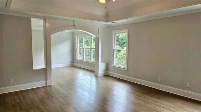 spare room with crown molding, wood finished floors, baseboards, and arched walkways