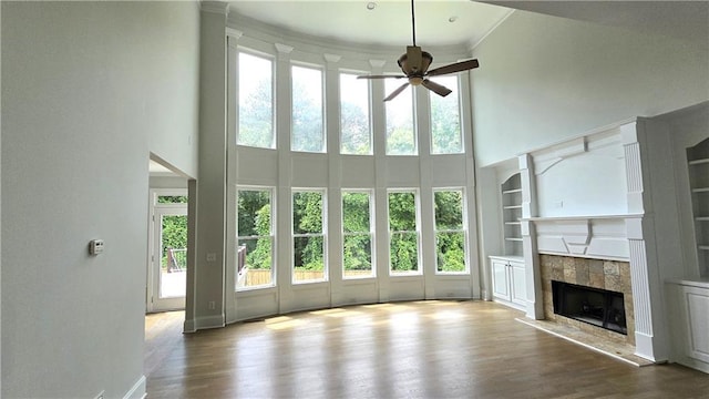 unfurnished living room with wood finished floors, a high ceiling, ceiling fan, and a tile fireplace