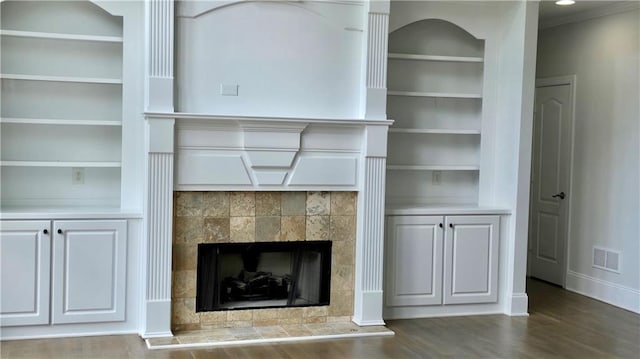 unfurnished living room with visible vents, built in shelves, wood finished floors, baseboards, and a tile fireplace