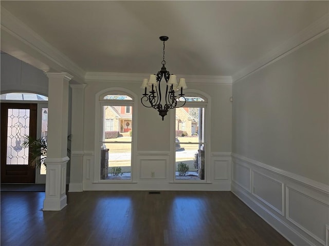 foyer with dark wood finished floors, decorative columns, ornamental molding, a decorative wall, and a chandelier