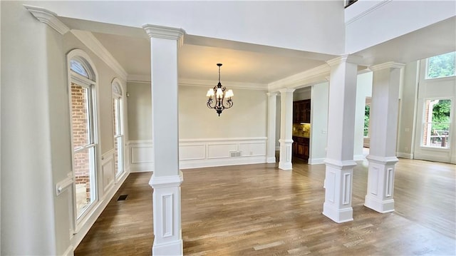 foyer entrance with visible vents, crown molding, wainscoting, wood finished floors, and a decorative wall