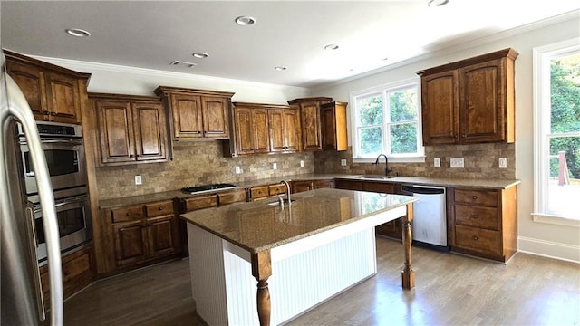 kitchen with a sink, stainless steel appliances, wood finished floors, and a kitchen island with sink