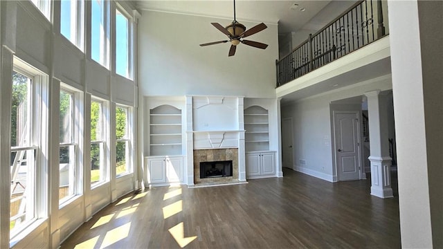 unfurnished living room with built in shelves, baseboards, ceiling fan, a fireplace, and wood finished floors