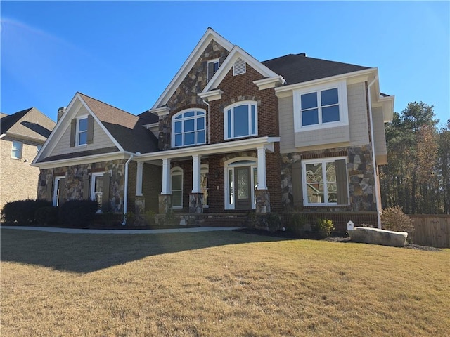 view of front of property featuring a front yard, a porch, brick siding, and stone siding