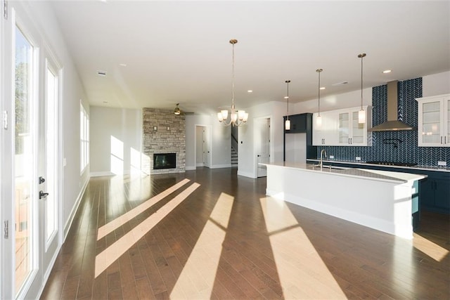 kitchen with sink, wall chimney exhaust hood, pendant lighting, decorative backsplash, and a center island with sink