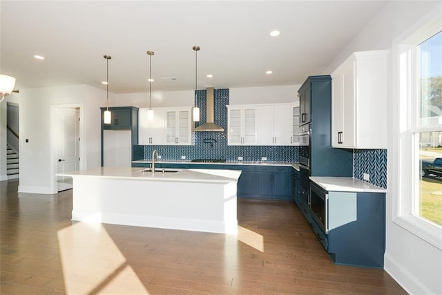 kitchen featuring sink, wall chimney range hood, tasteful backsplash, pendant lighting, and a kitchen island with sink