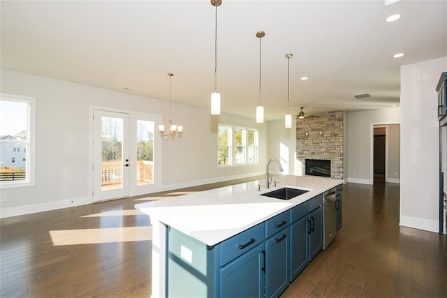 kitchen featuring stainless steel dishwasher, blue cabinets, sink, a center island with sink, and hanging light fixtures