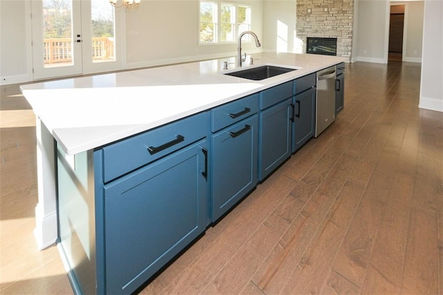 kitchen featuring sink, dishwasher, dark hardwood / wood-style flooring, blue cabinets, and a kitchen island with sink