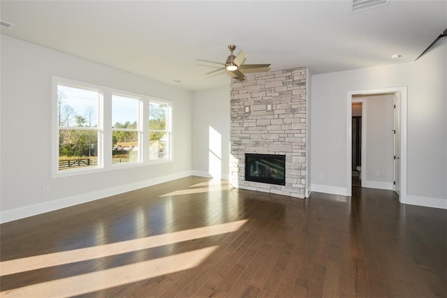 unfurnished living room featuring ceiling fan, a stone fireplace, and dark wood-type flooring