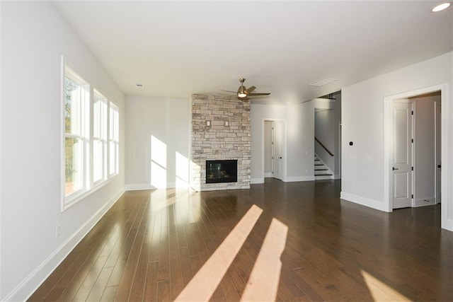 unfurnished living room featuring dark hardwood / wood-style flooring, a healthy amount of sunlight, a stone fireplace, and ceiling fan