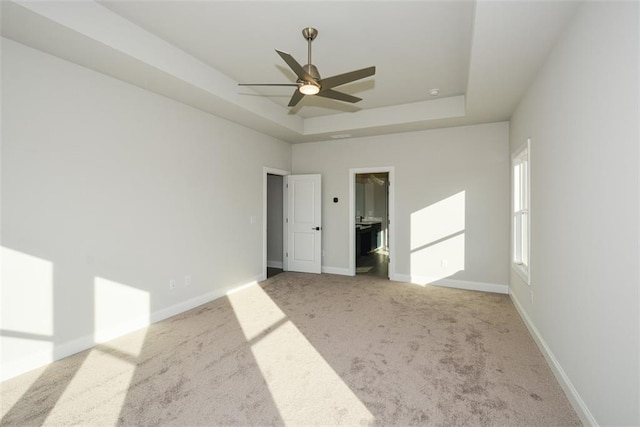 unfurnished bedroom with light carpet, a spacious closet, a raised ceiling, and ceiling fan