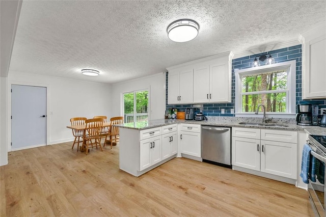 kitchen with a peninsula, tasteful backsplash, a sink, light wood finished floors, and appliances with stainless steel finishes