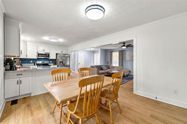 dining area featuring baseboards, a textured ceiling, ornamental molding, and light wood-style flooring