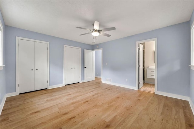 unfurnished bedroom featuring connected bathroom, multiple closets, baseboards, light wood-type flooring, and visible vents