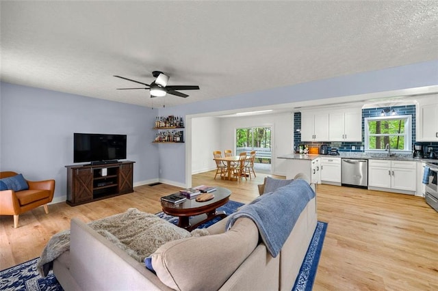 living area with baseboards, a ceiling fan, light wood finished floors, and a textured ceiling