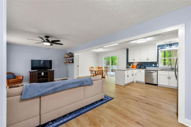 living room with ceiling fan, light wood finished floors, and a textured ceiling