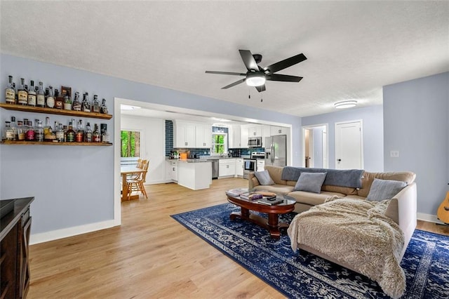 living room with a ceiling fan, baseboards, a textured ceiling, and light wood-type flooring