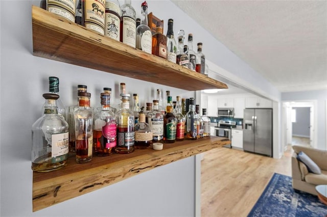 bar featuring stainless steel appliances, a dry bar, and light wood-style flooring