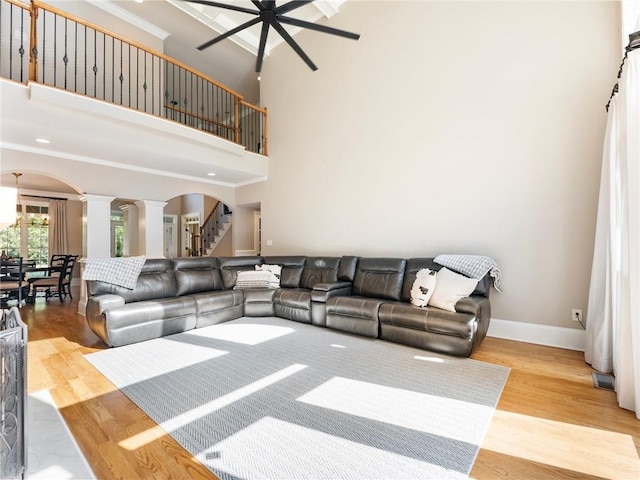 living room with ornate columns, a towering ceiling, hardwood / wood-style flooring, ornamental molding, and ceiling fan