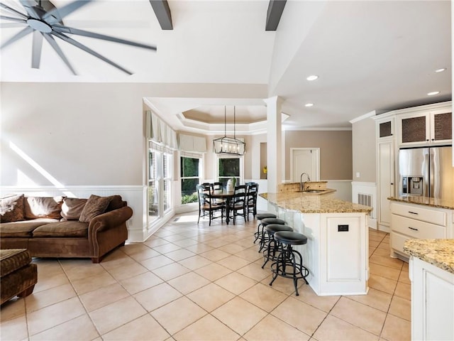 kitchen featuring a breakfast bar area, hanging light fixtures, light stone countertops, a center island with sink, and stainless steel fridge with ice dispenser