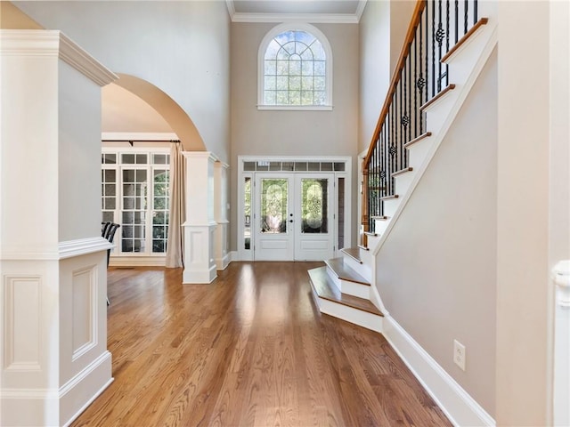 foyer entrance featuring french doors, wood-type flooring, ornamental molding, decorative columns, and a high ceiling