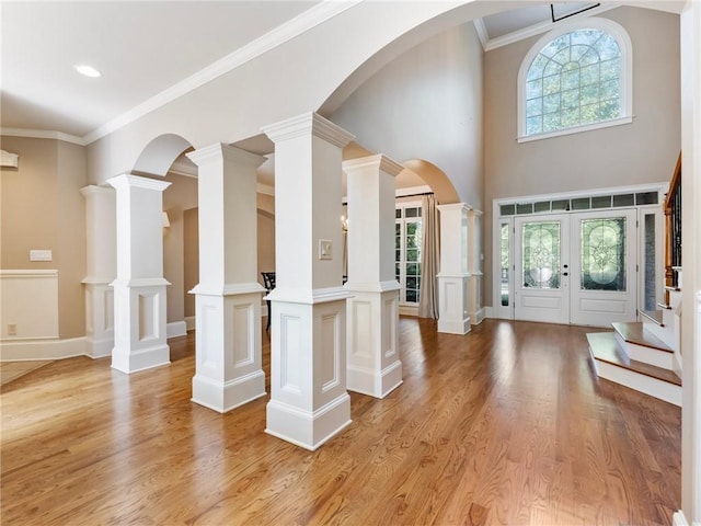 entryway with ornamental molding, decorative columns, and light wood-type flooring