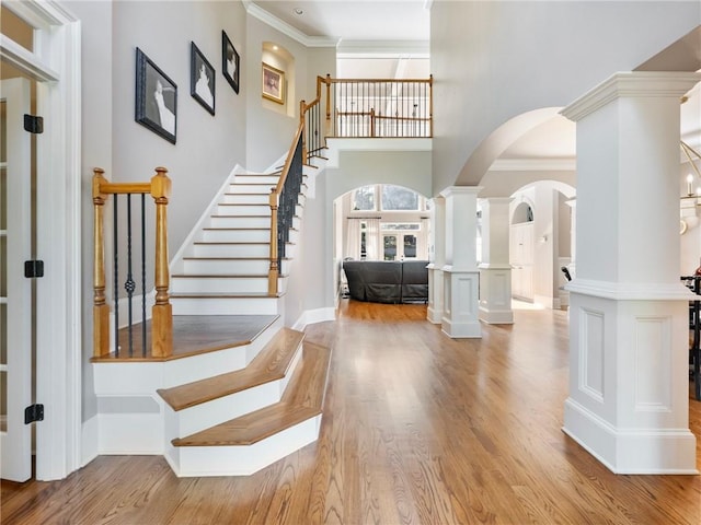 foyer with decorative columns, ornamental molding, a high ceiling, and light hardwood / wood-style flooring