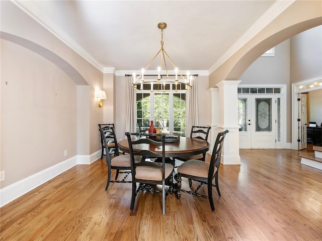 dining room with ornate columns, crown molding, a notable chandelier, and light hardwood / wood-style flooring