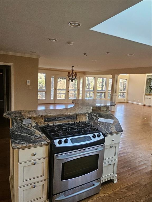 kitchen featuring a notable chandelier, stainless steel gas range oven, crown molding, and dark stone counters