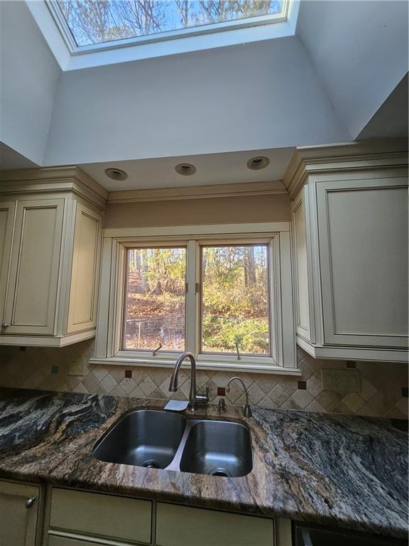 kitchen with vaulted ceiling with skylight, tasteful backsplash, and sink