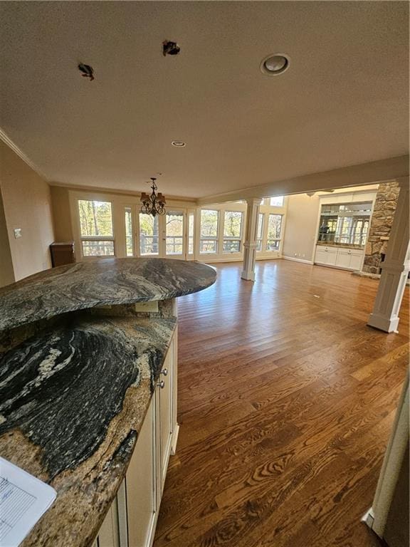 kitchen featuring white cabinetry, dark stone countertops, a chandelier, wood-type flooring, and ornamental molding