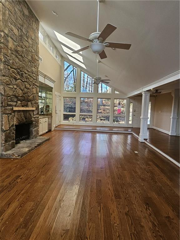 unfurnished living room featuring high vaulted ceiling, ceiling fan, a fireplace, wood-type flooring, and decorative columns