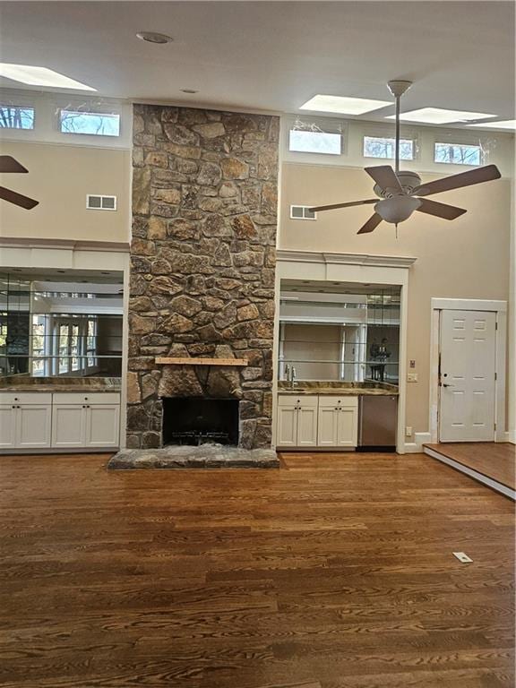 unfurnished living room with dark wood-type flooring, a fireplace, a towering ceiling, and a healthy amount of sunlight