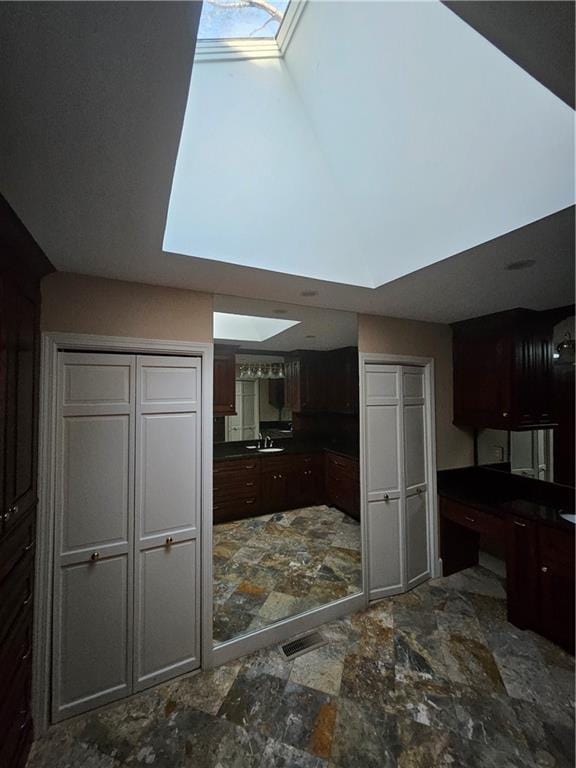 kitchen with dark brown cabinetry, a skylight, and sink