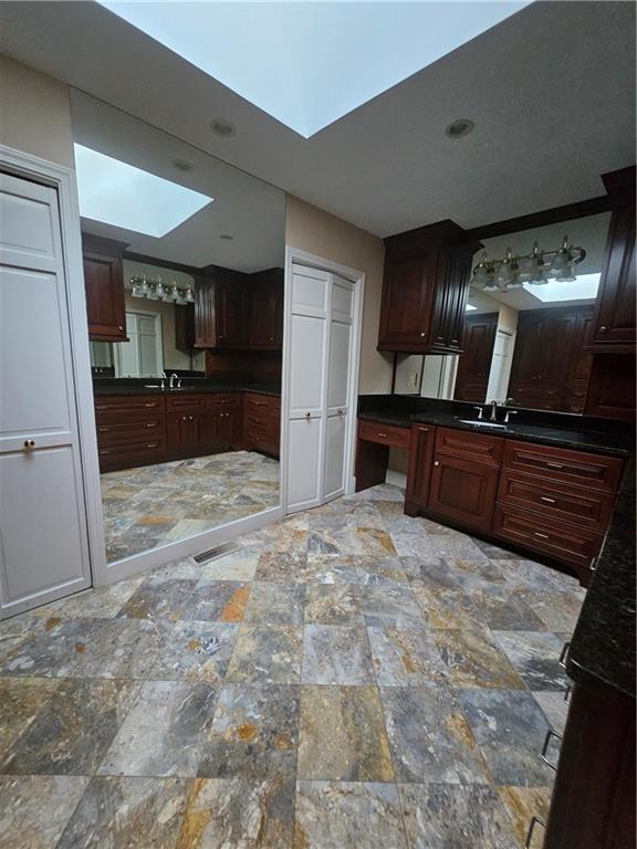 kitchen with a skylight, dark brown cabinetry, and sink