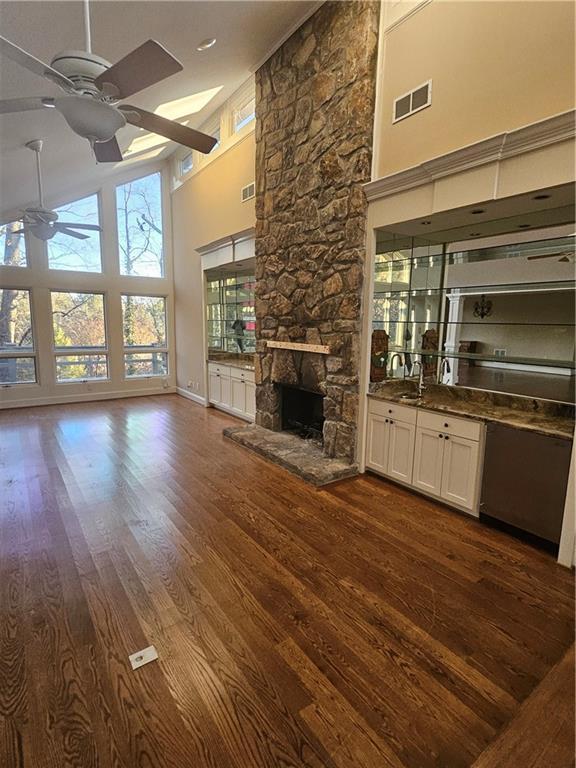 unfurnished living room featuring a towering ceiling, a stone fireplace, ceiling fan, and dark wood-type flooring